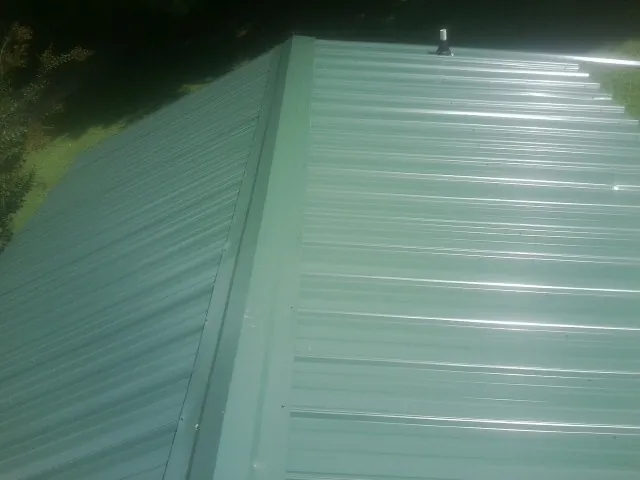 New green metal panels meeting at the ridge of a roof — Flat Roof Repair work by our crew in Macomb