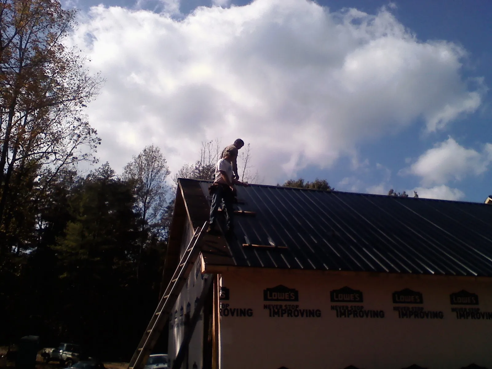 Roofer fastening dark metal panels high against a cloudy sky, from a Roof Inspection job in Macomb